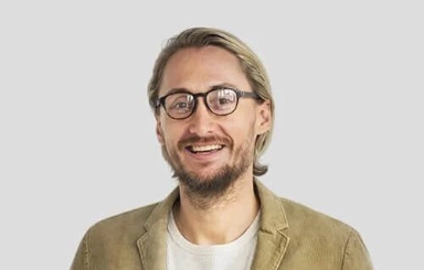 Smiling man in a blue shirt with arms crossed in front of a white background.